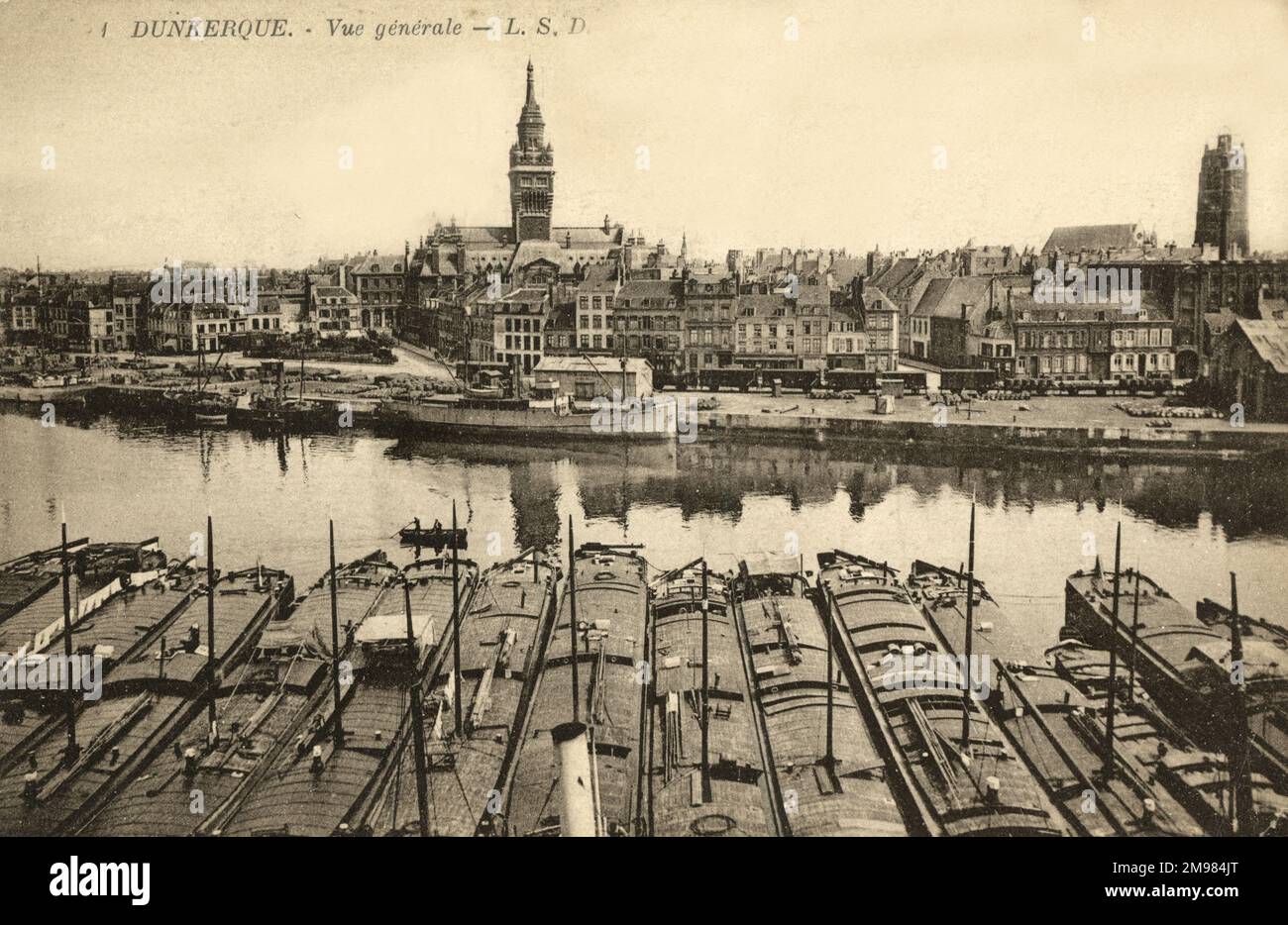 Dunkirk, France - a view out over the harbour, showing tethered fishing boats in the foreground and the town hall a a church belfry in the distance. Stock Photo