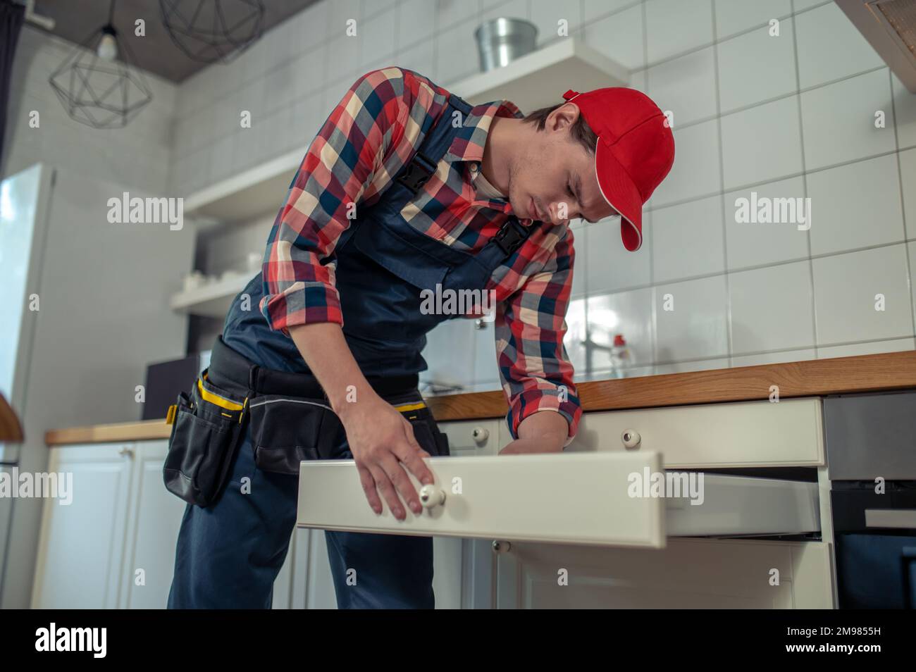 Calm focused repairman dressed in workwear attaching the knob to the