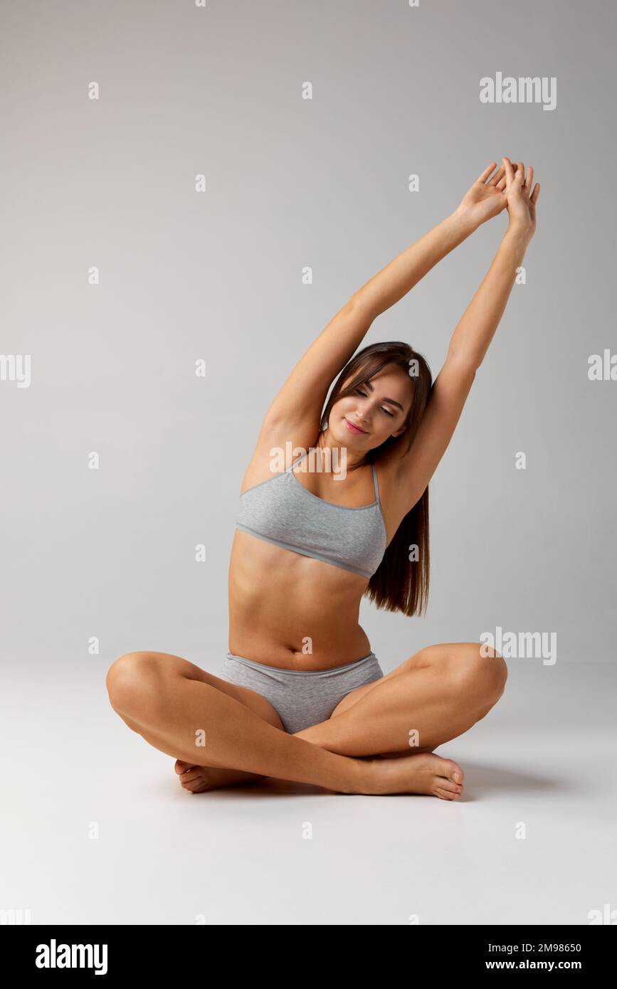 Stretching, yoga. Portrait of young beautiful girl posing in underwear over grey studio background. Concept of body and skin care, fitness Stock Photo