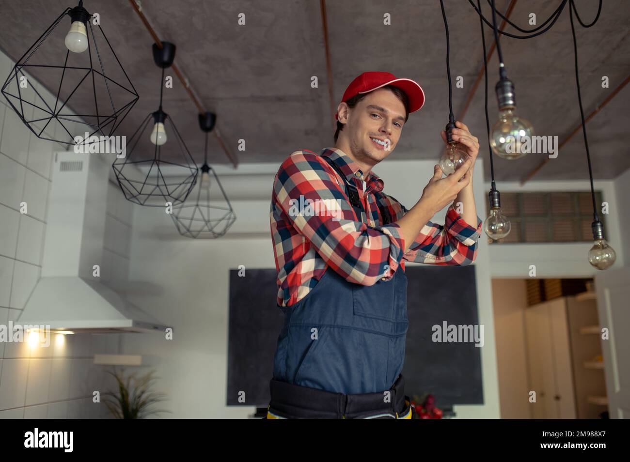 Experienced young Caucasian repairman with a radiant smile screwing the electric bulb into the socket Stock Photo