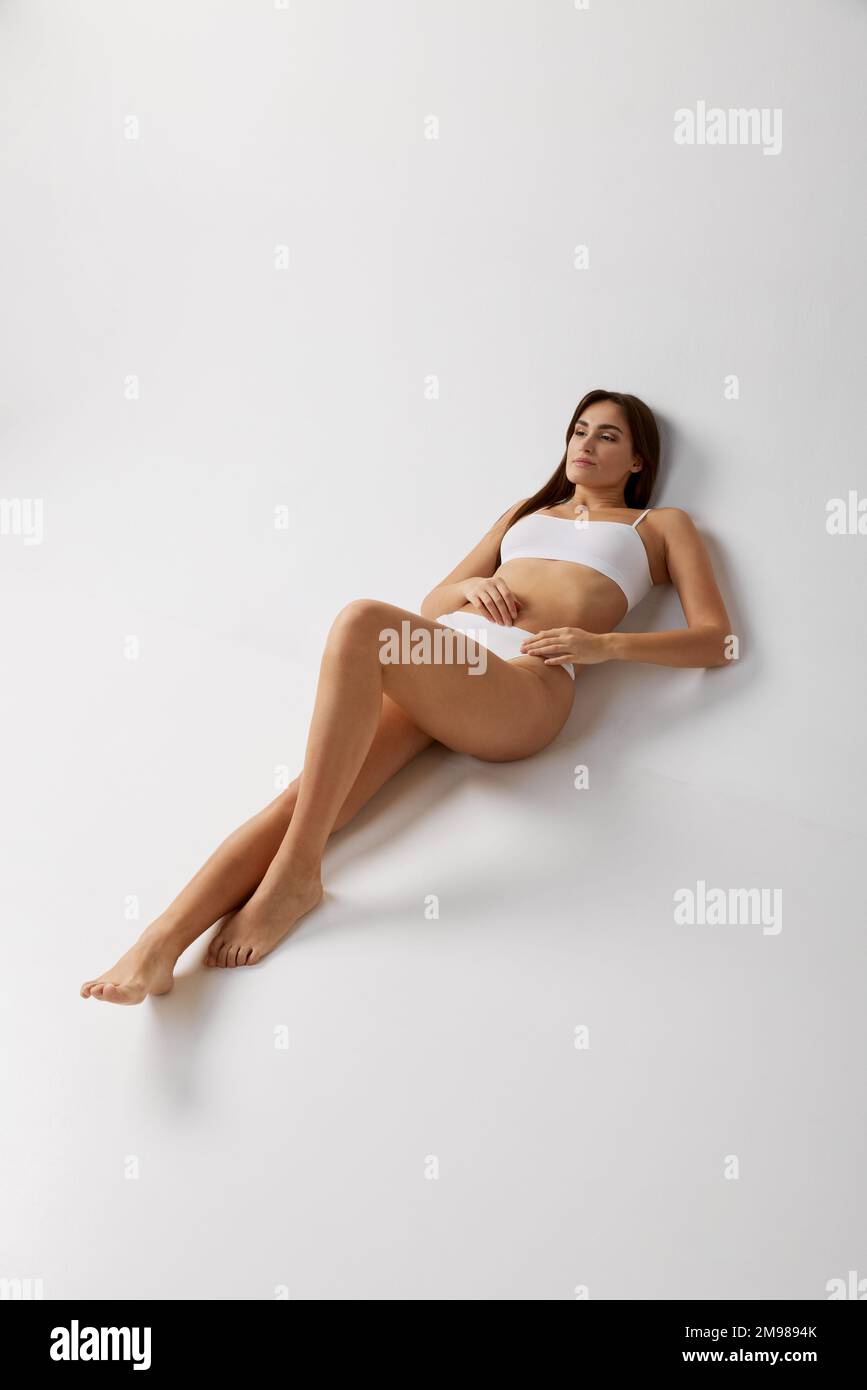 Portrait of young beautiful girl posing in white underwear over grey studio background. Slender body. Concept of body and skin care, fitness Stock Photo
