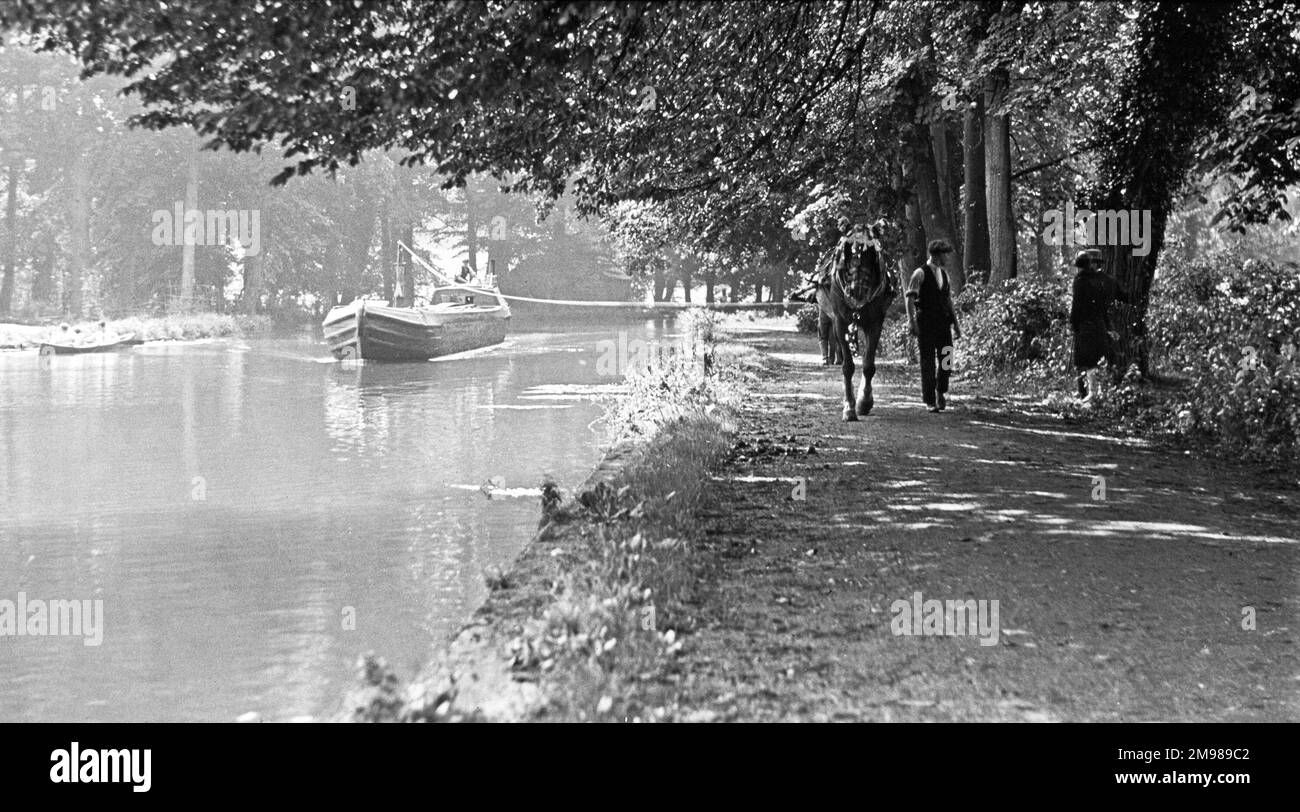 Canal boat drawn by a horse, led by a man along a towpath Stock Photo