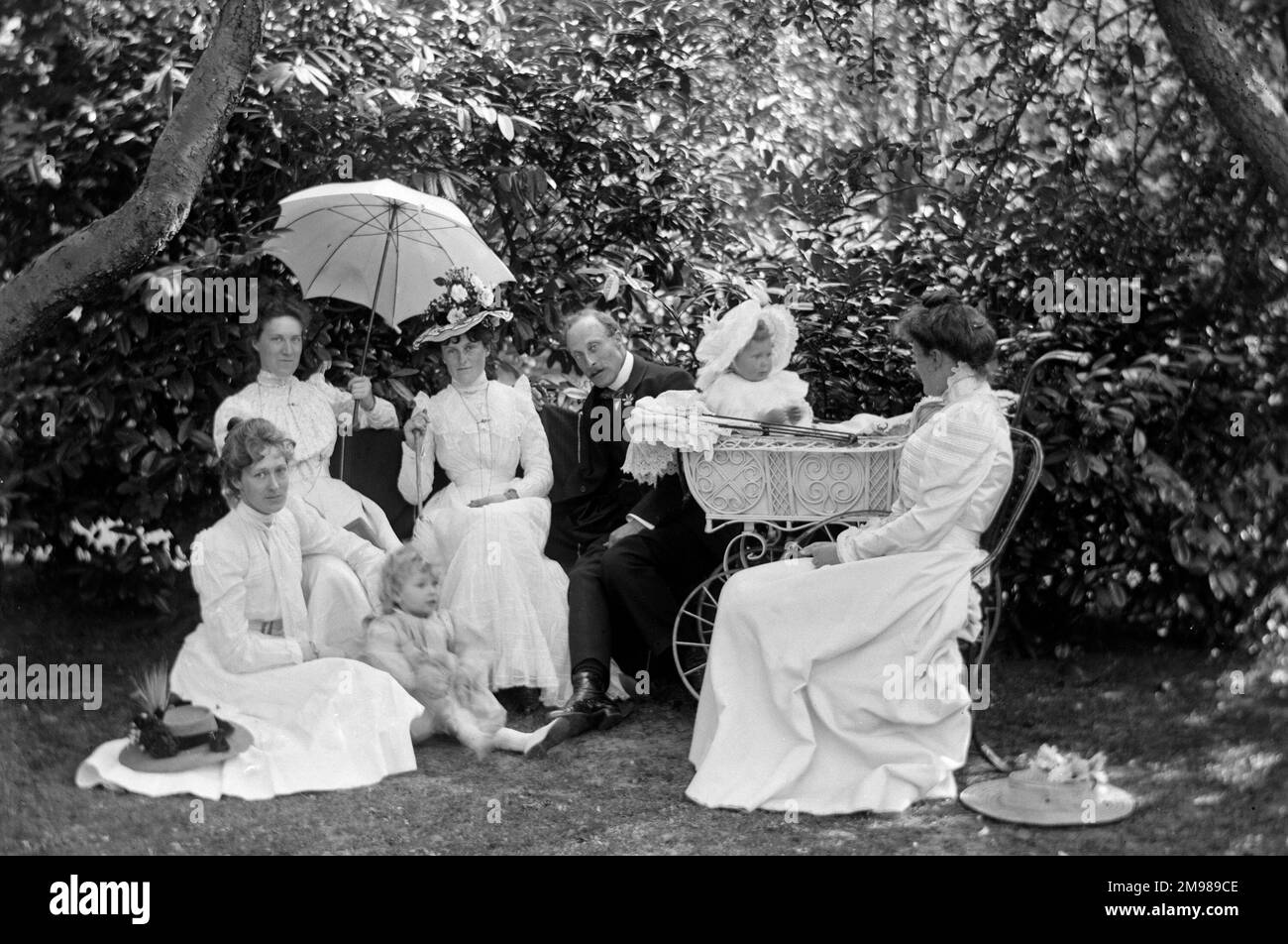 Family group with a baby in a pram and a seated child in the garden of The Grove, Bamford, Derbyshire, England. Stock Photo
