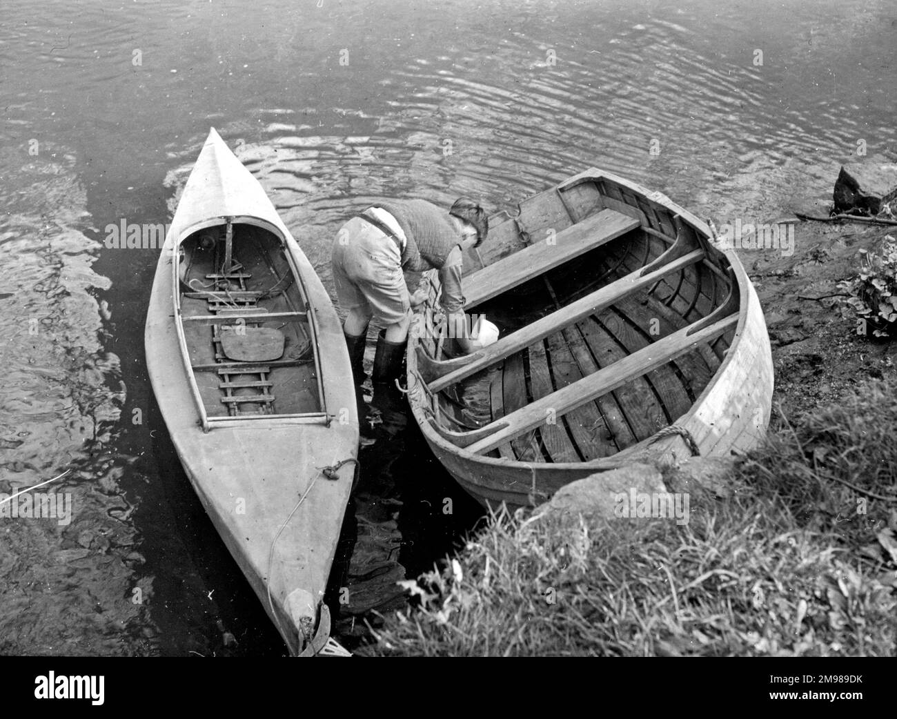 Boy bailing out water from a rowing boat, with a canoe alongside. Stock Photo