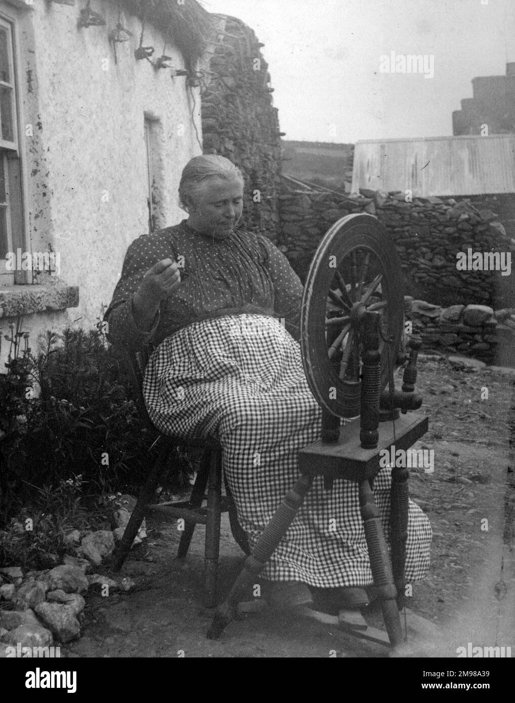 Woman outside her cottage spinning wool in Glen Columbkille (Glencolmcille, Gleann Cholm Cille), County Donegal, north-west Ireland. Stock Photo