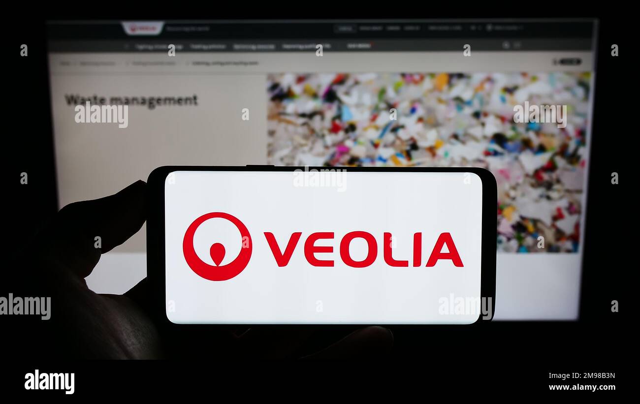Person holding smartphone with logo of French company Veolia Environnement S.A. on screen in front of website. Focus on phone display. Stock Photo