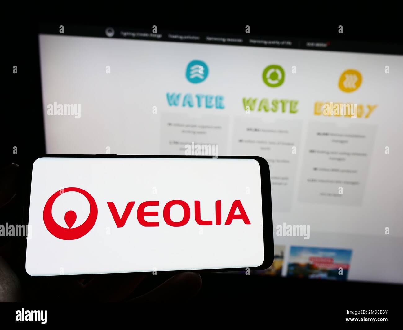 Person holding cellphone with logo of French company Veolia Environnement SA on screen in front of business webpage. Focus on phone display. Stock Photo