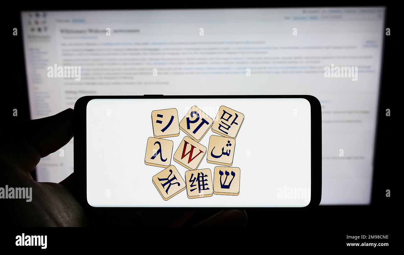 Person holding cellphone with logo of online dictionary Wiktionary (Wikimedia) on screen in front of webpage. Focus on phone display. Stock Photo