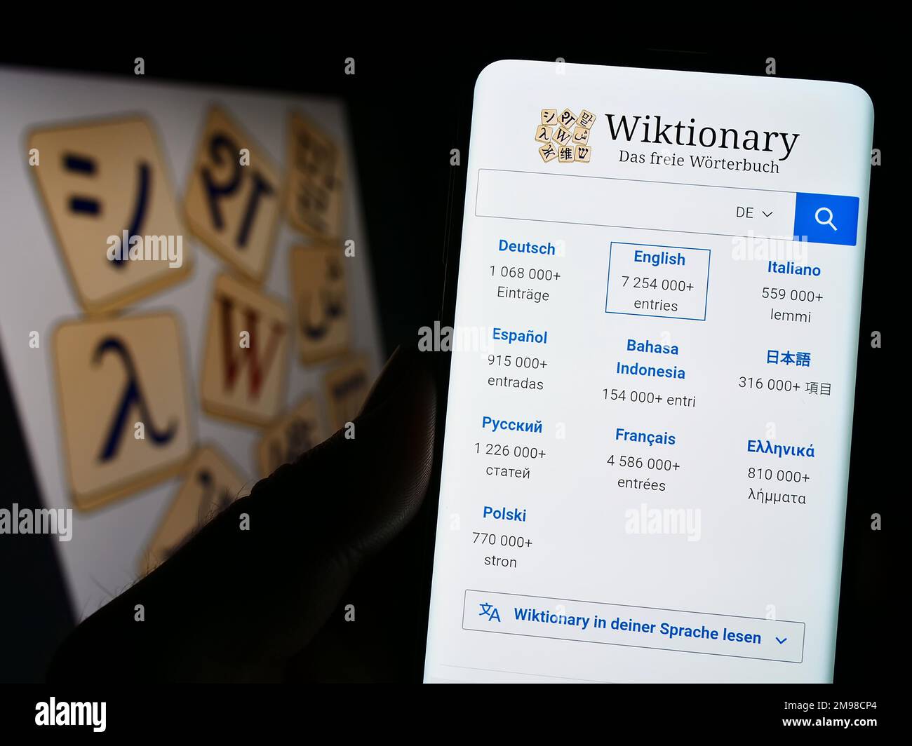 Person holding cellphone with website of online dictionary Wiktionary (Wikimedia) on screen in front of logo. Focus on center of phone display. Stock Photo