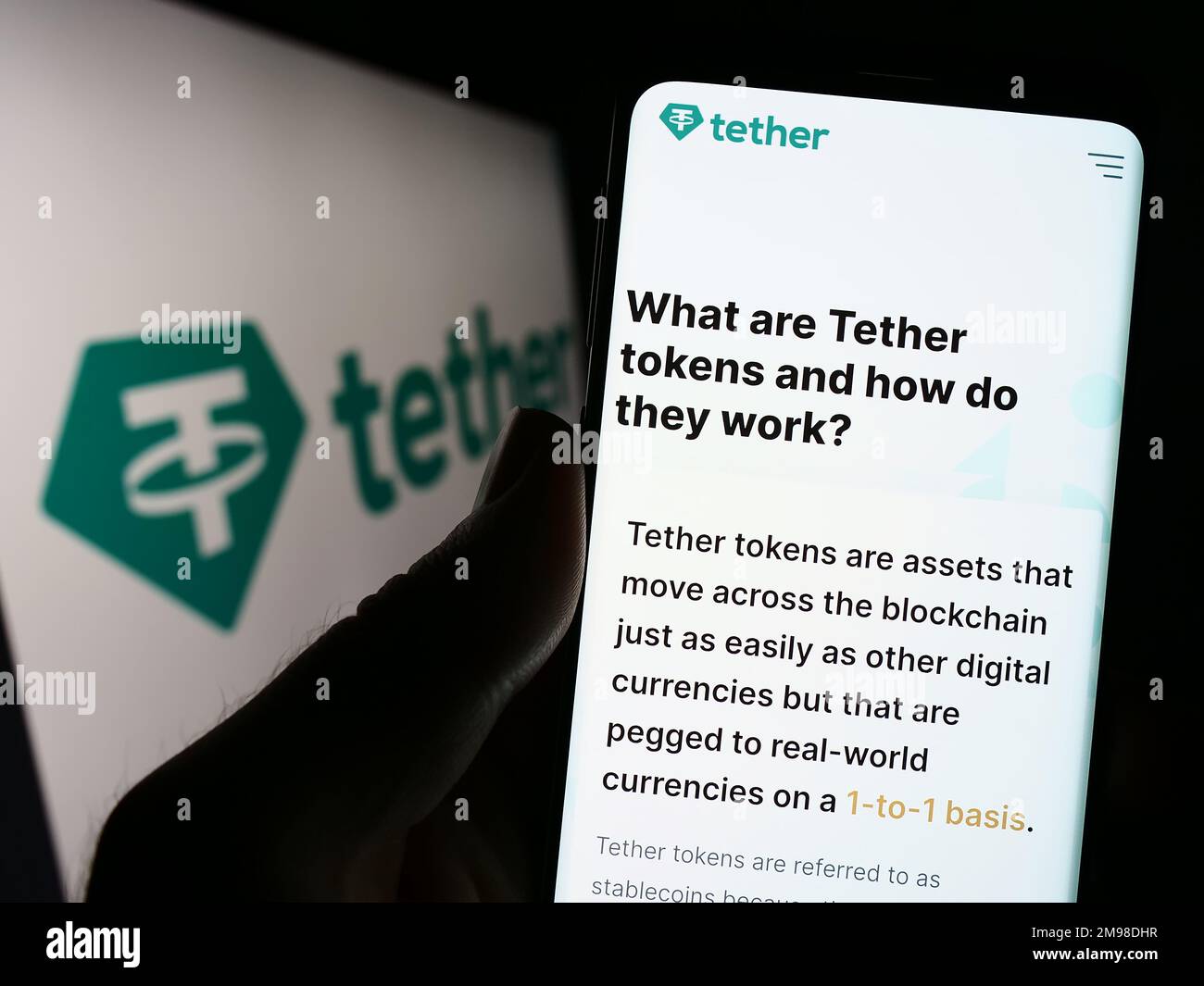 Person holding cellphone with webpage of crypto company Tether Operations Limited on screen in front of logo. Focus on center of phone display. Stock Photo