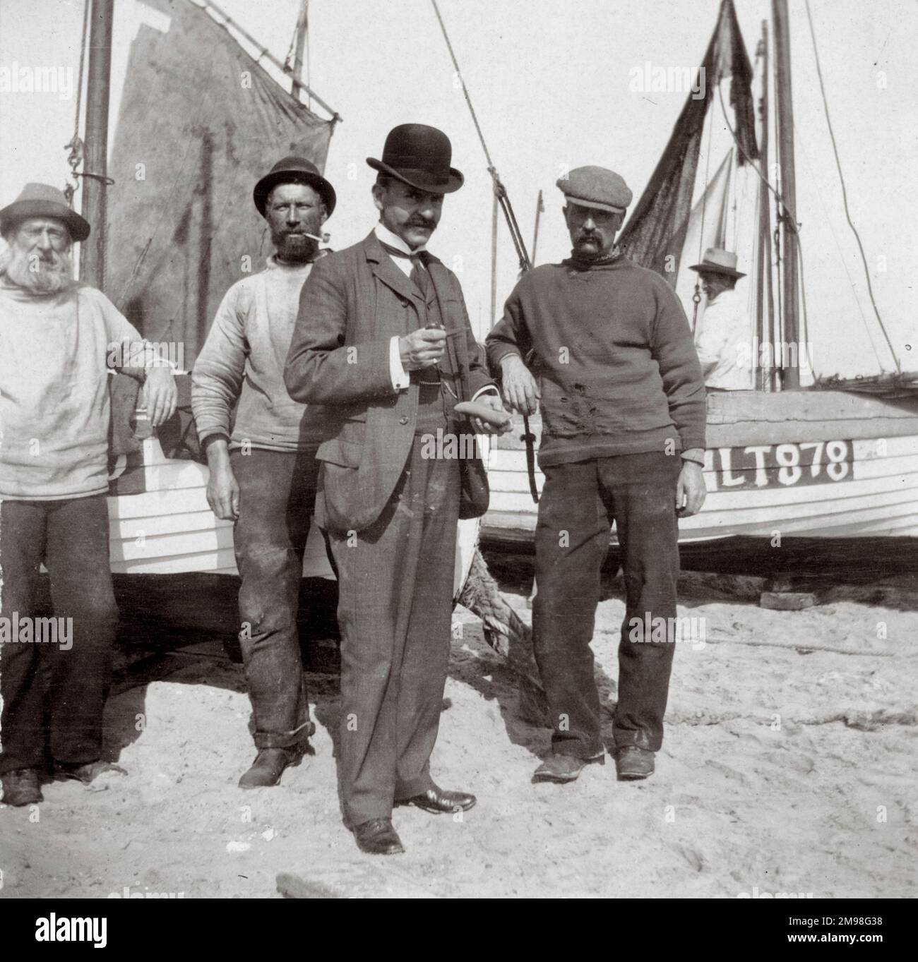 Fishermen Denny, Rogers, Craigie and Peck, on the beach with boats, Southwold, Suffolk.  The man in the suit and bowler hat is Arthur Auerbach. Stock Photo