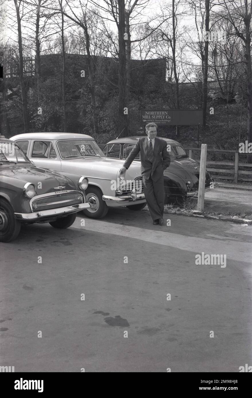 1950s, historical, a man in a suit standing outside a motor sales business with cars of the era, a Hillman and Ford Zephyr Mark II, at Hargood Motor Sales, Wilmslow Rd, Parrs Wood, Didsbury, Manchester, England, UK. Sign in the front window of the Zephyr says 'For Sale'. Stock Photo