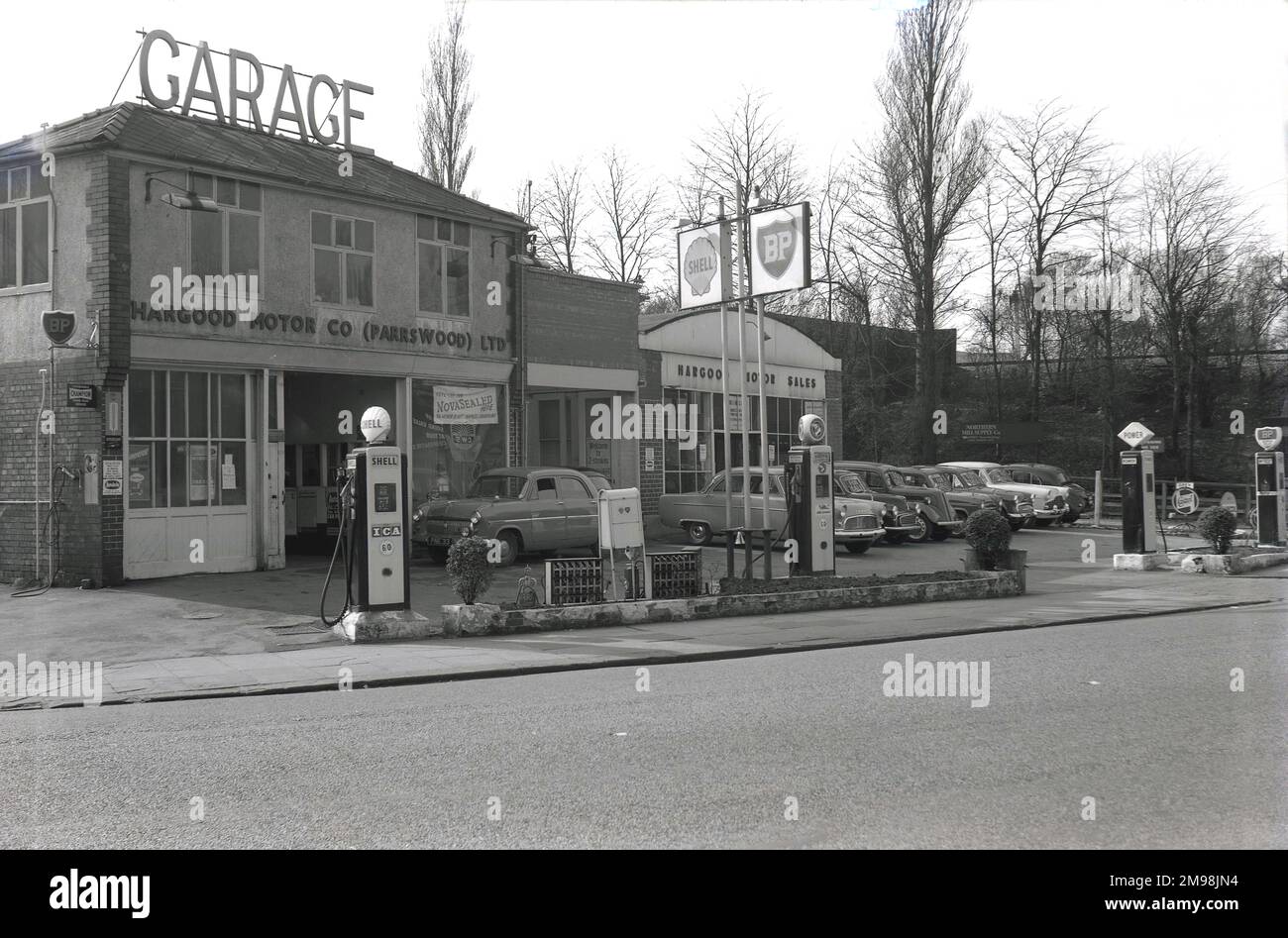 1957, historical, exterior of the Hargood Motor Co on the Wilmslow Rd, Didsbury, Manchester, England, UK. The word Garage is displayed in large capital letters on the roof of the two-storey building and cars of the day are parked outside the motor sales dept on the right of the picture. As can be seen by the signs and the forecourt petrol pumps, different brands of fuel including BP, Shell, Power and National, were offered to the motorist of this era. Stock Photo