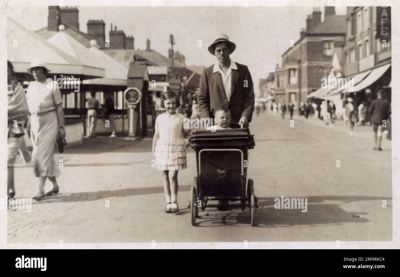 Mablethorpe, Lincolnshire - Gent pushing his young baby boy, sitting up in a fine perambulator ('Redelsham'?) with his elder daughter in a  pretty white summer dress, walking alongside. Stock Photo