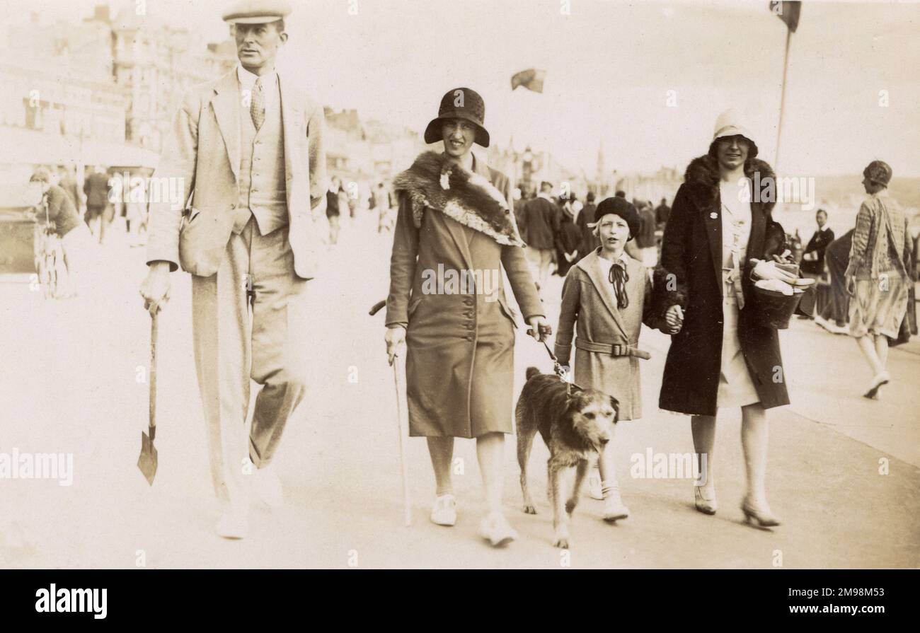 Family (and pet dog) on holiday in Weymouth, Dorset - candid seaside photograh taken as they strolled along the front (Brunswick Terrace). Father does not seem to be too happy about being photographed in this manner as he lopes along grudgingly carrying the children's spade... Stock Photo