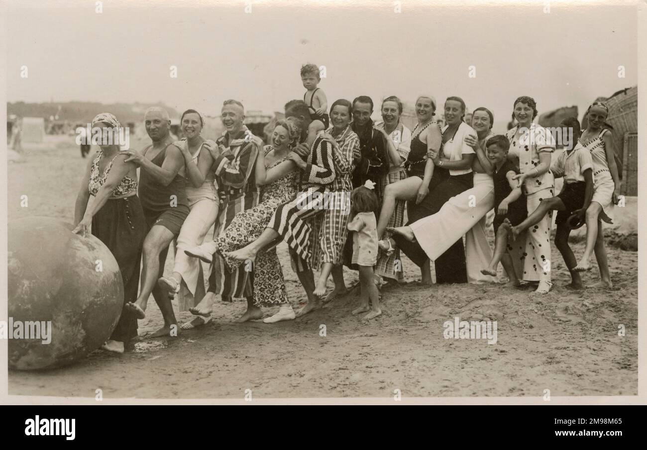 A wonderful photograph of a very jolly group (possibly one large extended family) playing with a huge ball on the beach - note the variety of magnificent beachwear on show!! Encapsulating the joy of the British seaside holiday in one image... Stock Photo