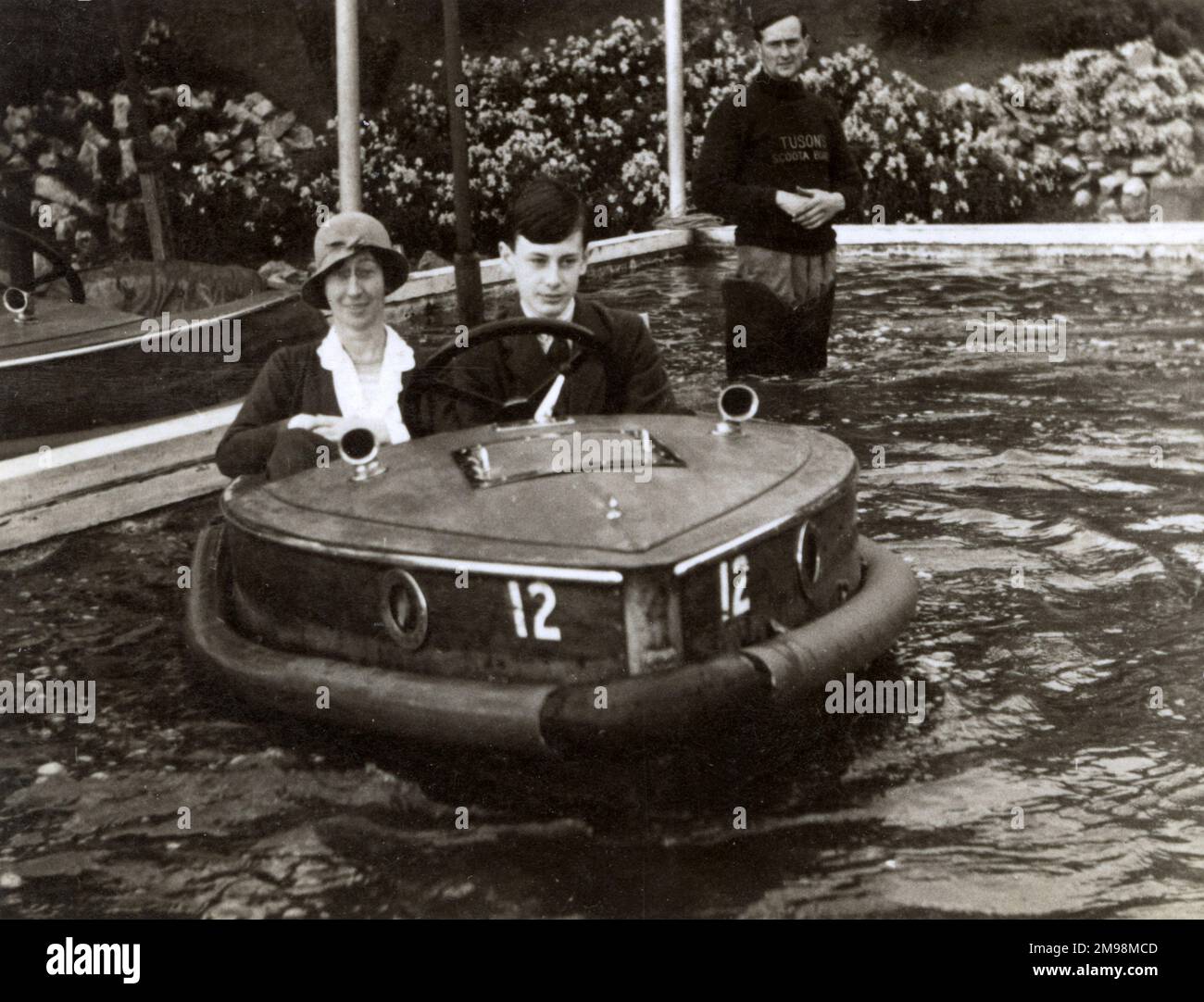 Mother and son riding a Rytecraft Scoota-boat - a wooden plywood motor boat at the Fairground - Tuson's Scoota Boats - Llandudno, Wales. These boats are the electric type with 110 volt motor, powered from a mesh up above, earthing out through the water. Stock Photo