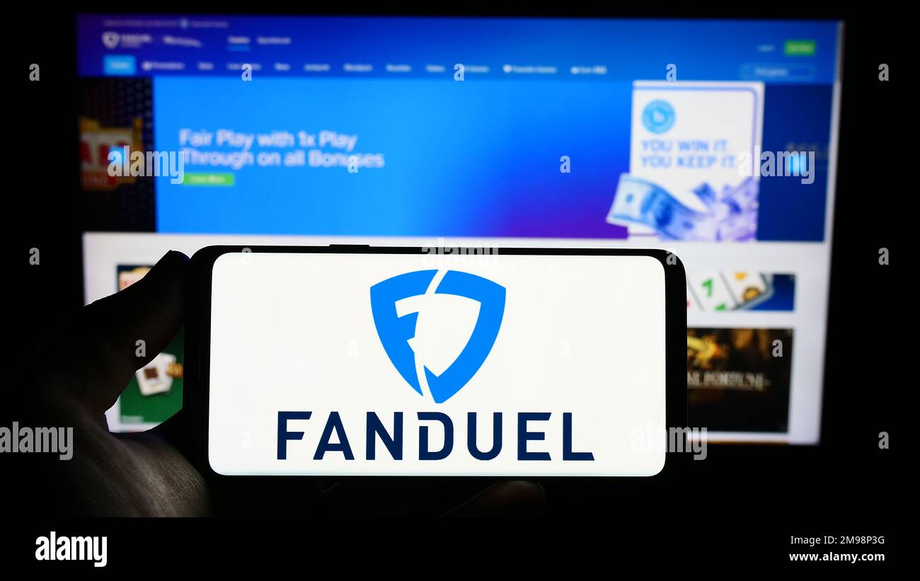 Person holding smartphone with logo of US gambling company FanDuel Inc. on screen in front of website. Focus on phone display. Stock Photo