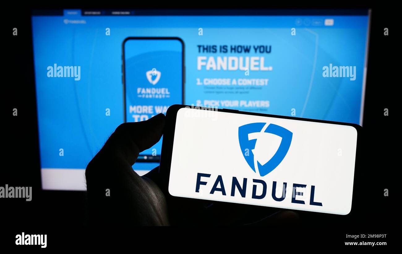 Person holding mobile phone with logo of American gambling company FanDuel Inc. on screen in front of business web page. Focus on phone display. Stock Photo