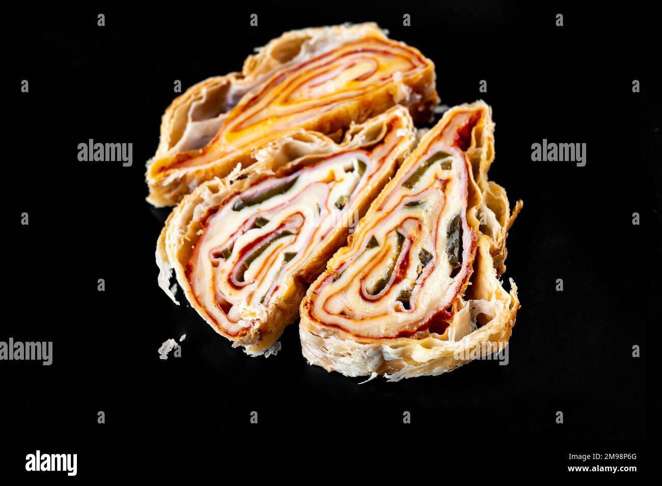 Three piece of sliced salty rolled pastry with ham, cheese and jalapenos on black background, closeup. Nice layers of food on the cut. Appetizer, snac Stock Photo