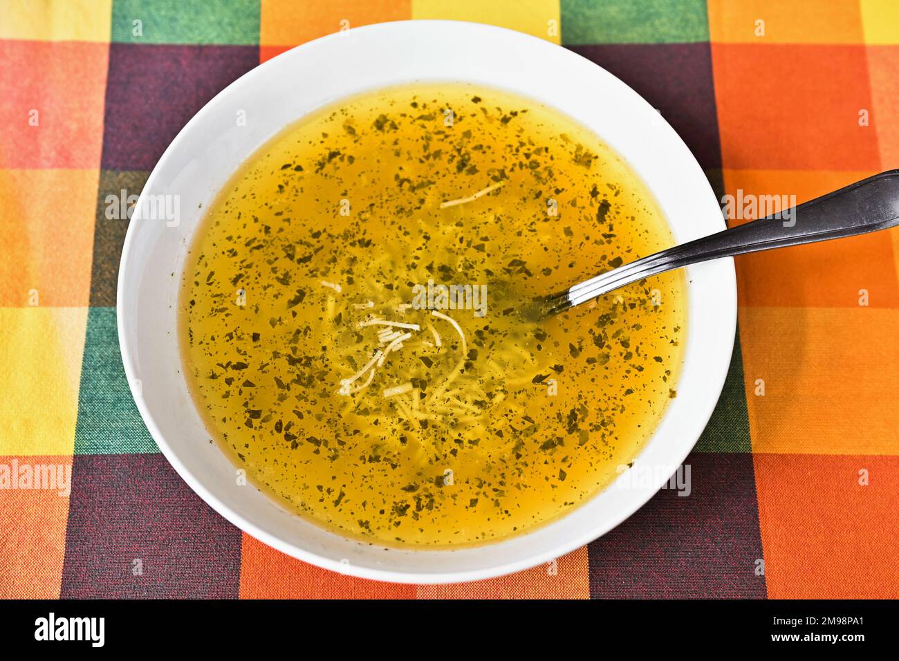 Noodle soup with herb in white plate on orange tablecloth, closeup. Stock Photo