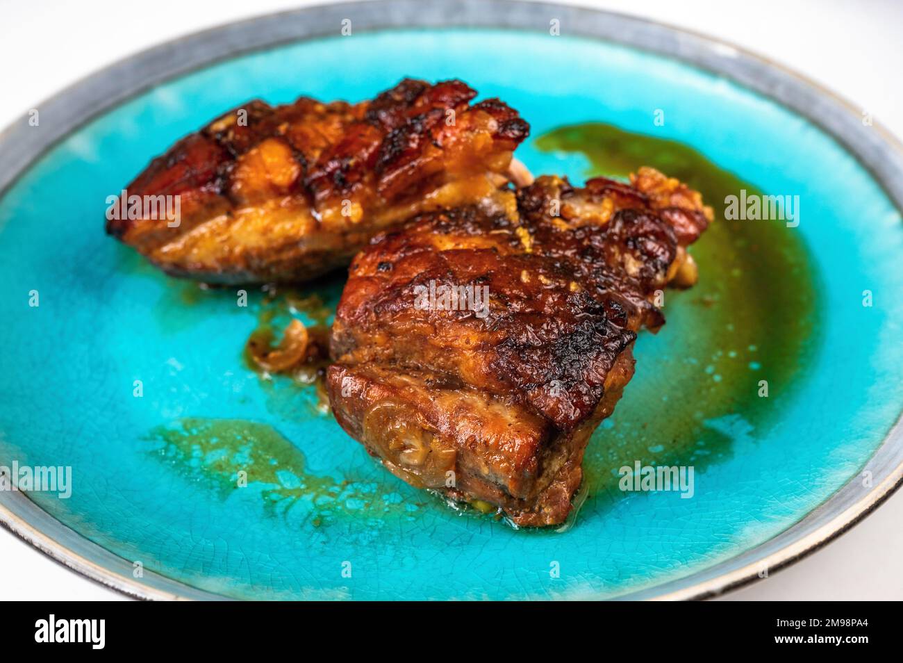 Two piece of baked pork belly with crispy skin on blue plate, closeup. Stock Photo