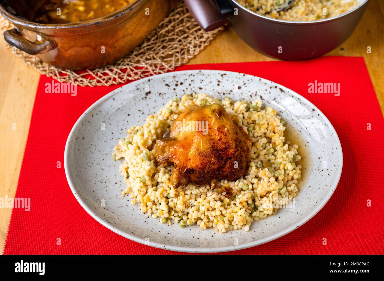 Baked chicken quarter with boiled tarhona (type of european pasta) on plate, pot on red background. Stock Photo