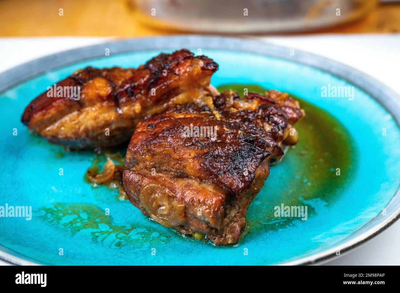 Two piece of baked pork belly with crispy skin on blue plate on table, closeup. Stock Photo