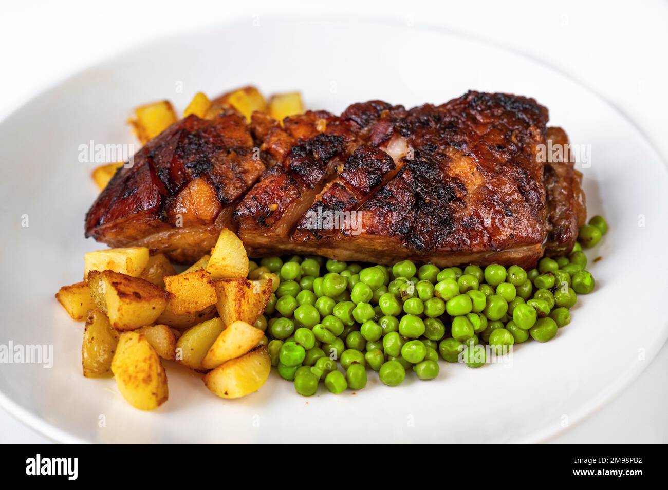 Baked fried pork belly with crispy skin and potato and pea on white plate, closeup. Stock Photo