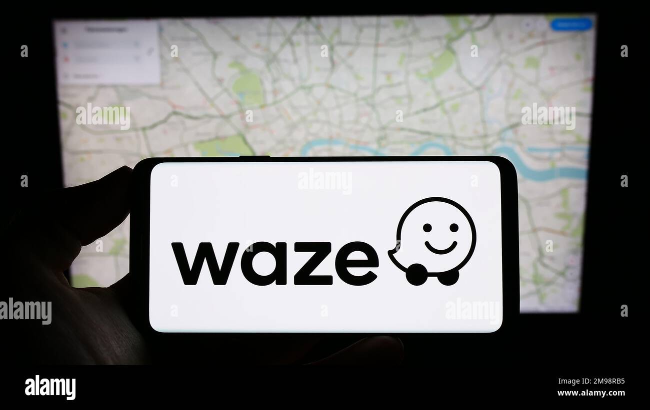 Person holding cellphone with logo of Israeli navigation company Waze Mobile Ltd. on screen in front of business webpage. Focus on phone display. Stock Photo