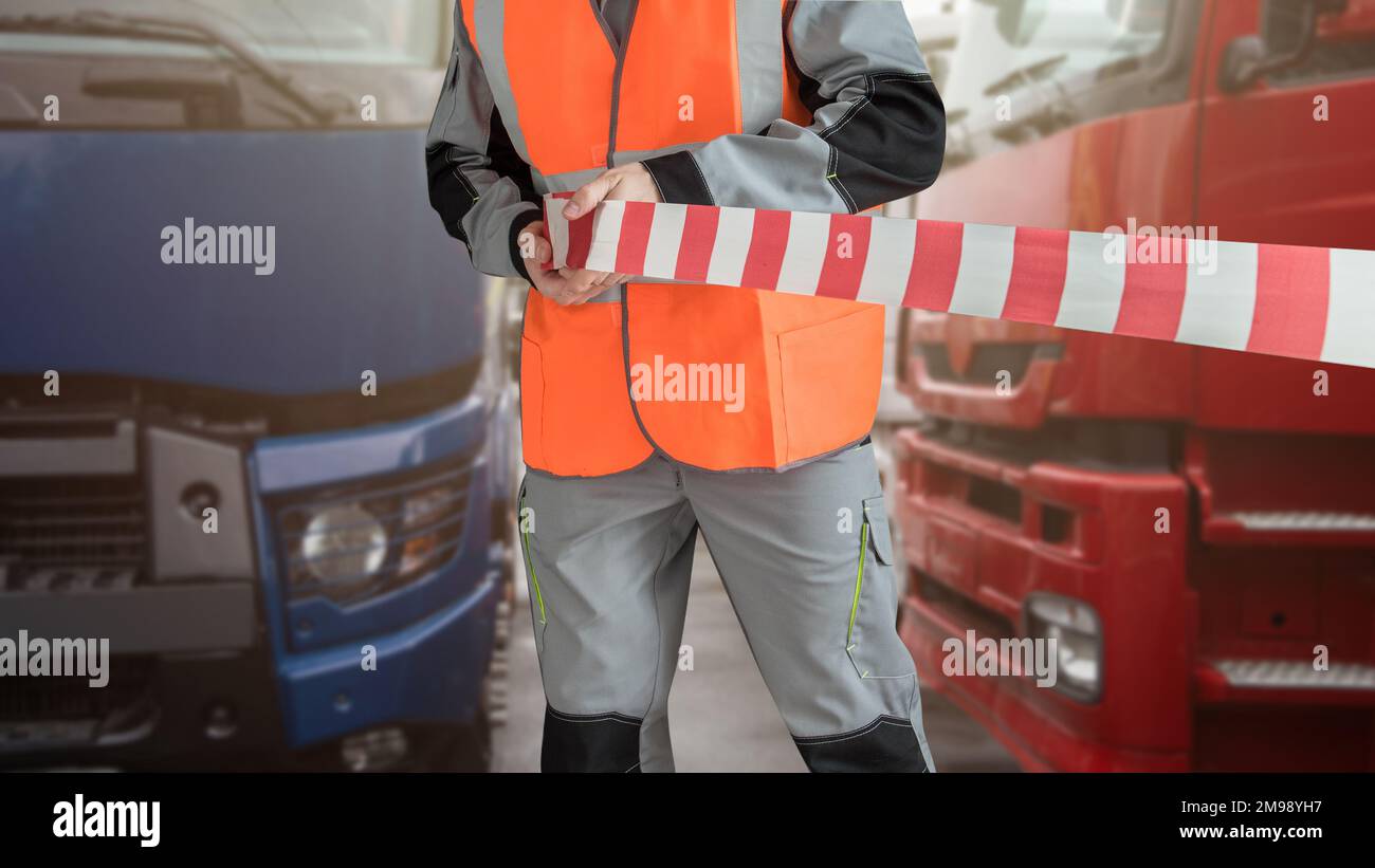 Man in special clothes blocks the parking with a tape. Different semi trucks on the background Stock Photo