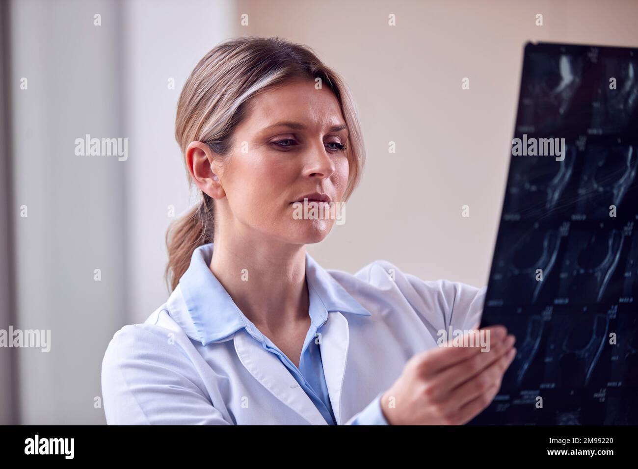 Female Doctor Wearing White Coat Standing In Hospital Corridor Looking At CT Or MRI Scan Stock