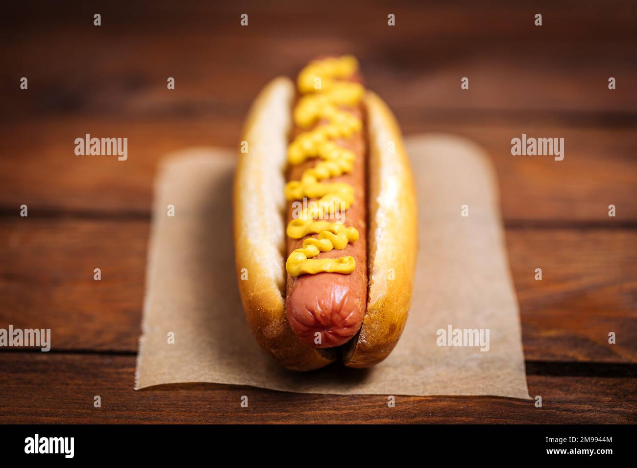 Classic fast food hot dog served with mustard on a rustic wooden board. Served with potato chips and sauces. Stock Photo