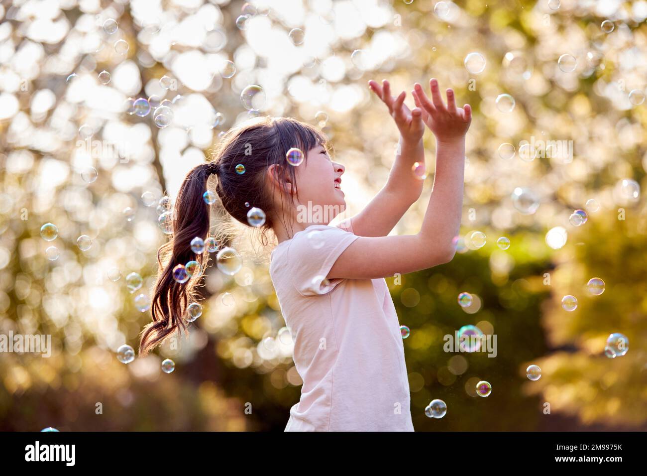 Smiling Girl Outdoors Having Fun Playing With Bubbles In Garden Stock Photo