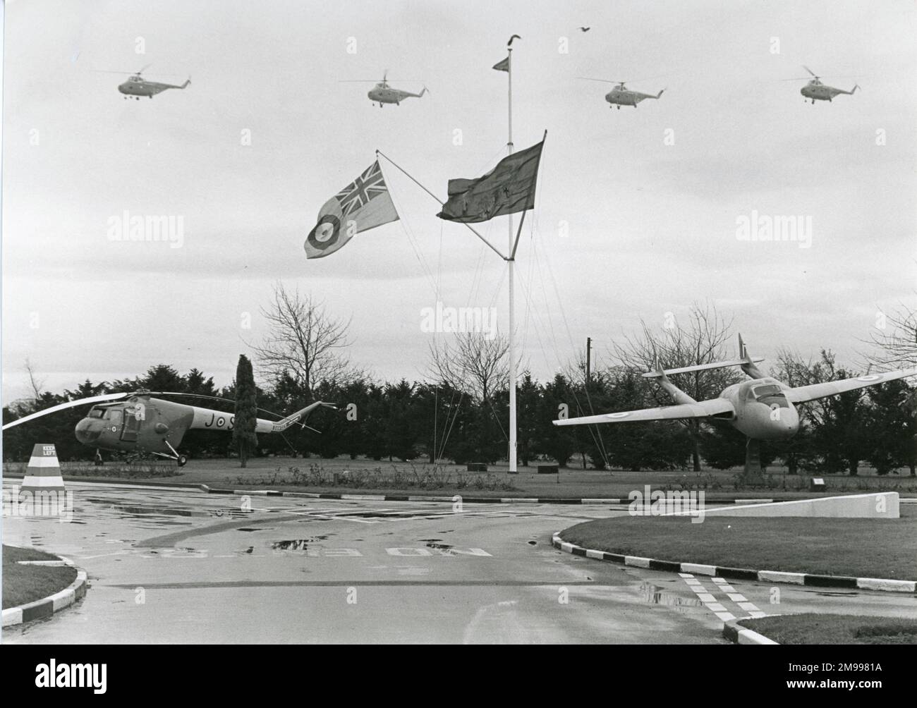 Four Westland Whirlwinds of No.2 Flying Training School, RAF Shawbury, near Shrewsbury, make a final flight over their base on 17 December 1980, to mark the withdrawal of the type from the training role after 26 years of service. The gate guardians are a Bristol Sycamore helicopter and a de Havilland Vampire T11. Stock Photo