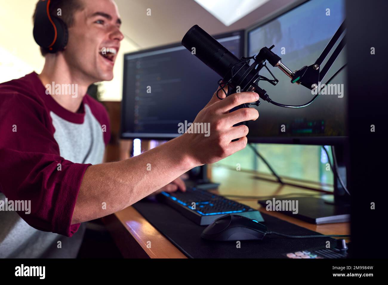Man Gaming At Home Wearing Wireless Headphones Sitting At Desk With Multiple Monitors Stock Photo