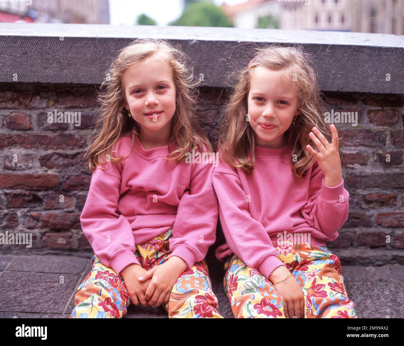Local identical twin girls sitting by wall, Lloret de Mar, Costa Brava, Province of Girona, Catalonia, Spain Stock Photo