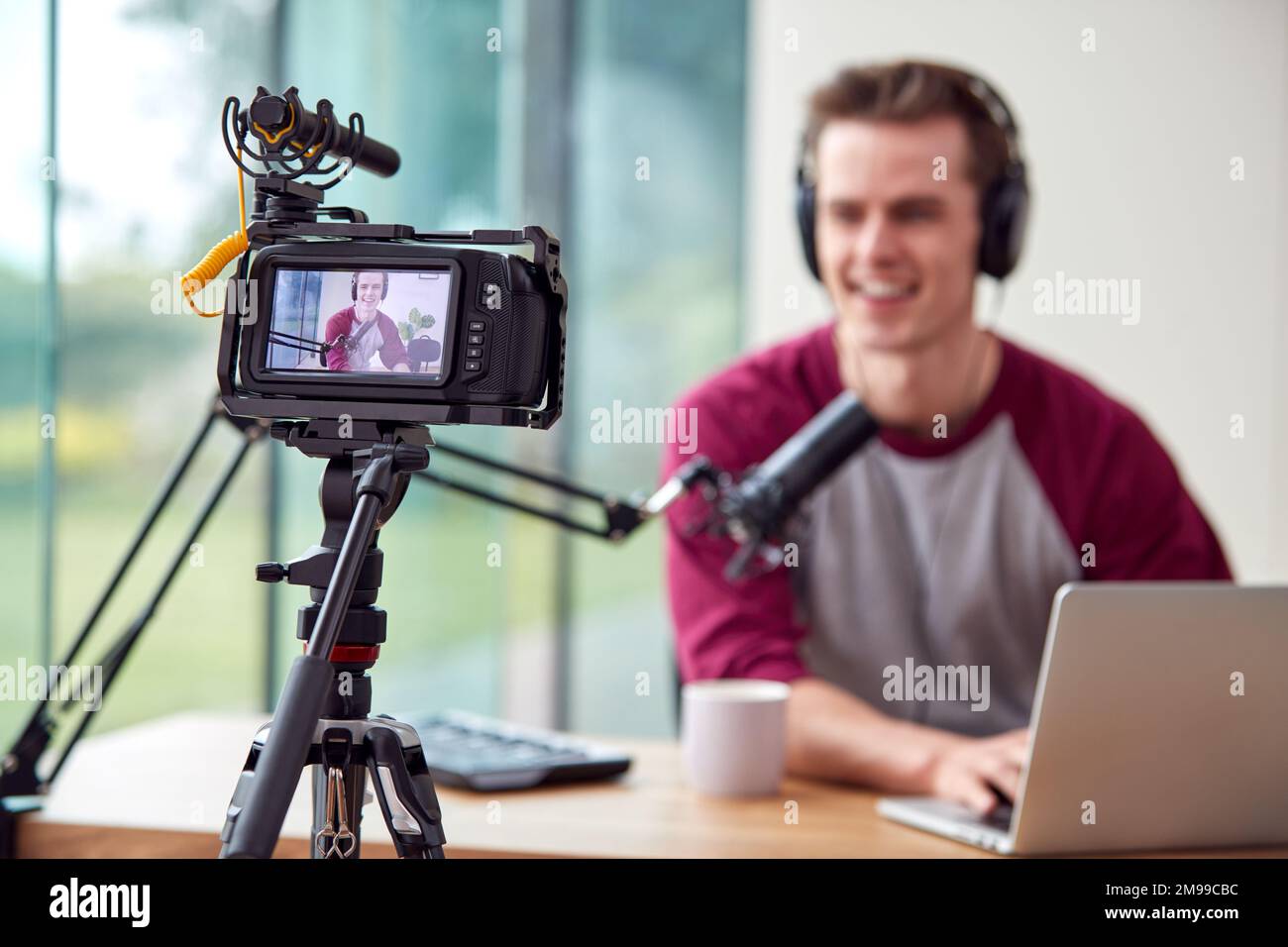 Male Vlogger With Laptop Recording Video At Home With Camera Stock Photo