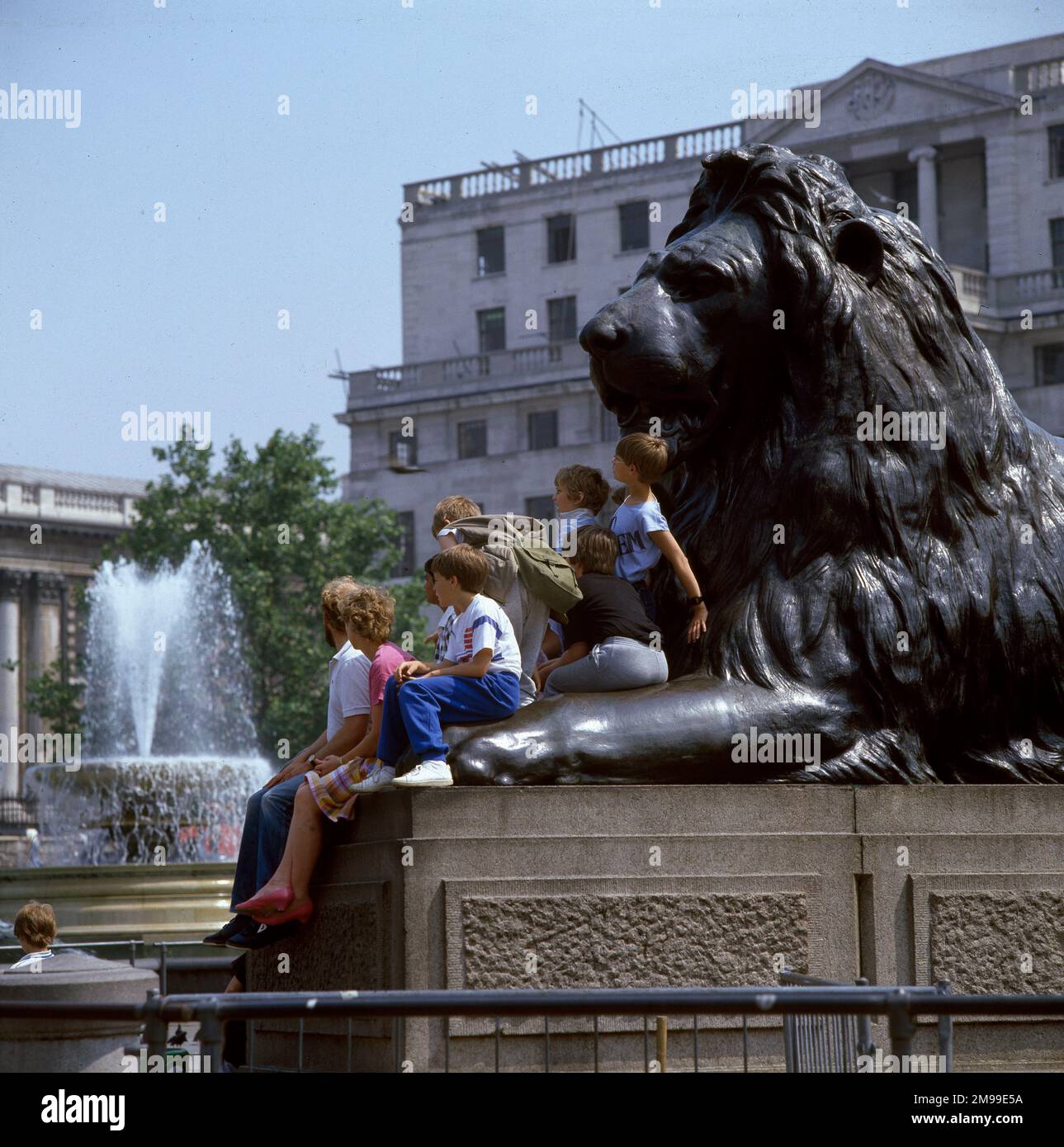 Children and adults sit on a Landseer Lion - Trafalgar Square, London. Stock Photo