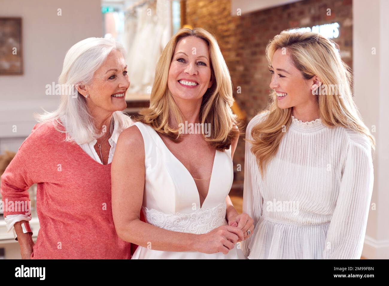 Portrait Of Grandmother With Adult Daughter And Granddaughter Trying On Wedding Dress In Store Stock Photo