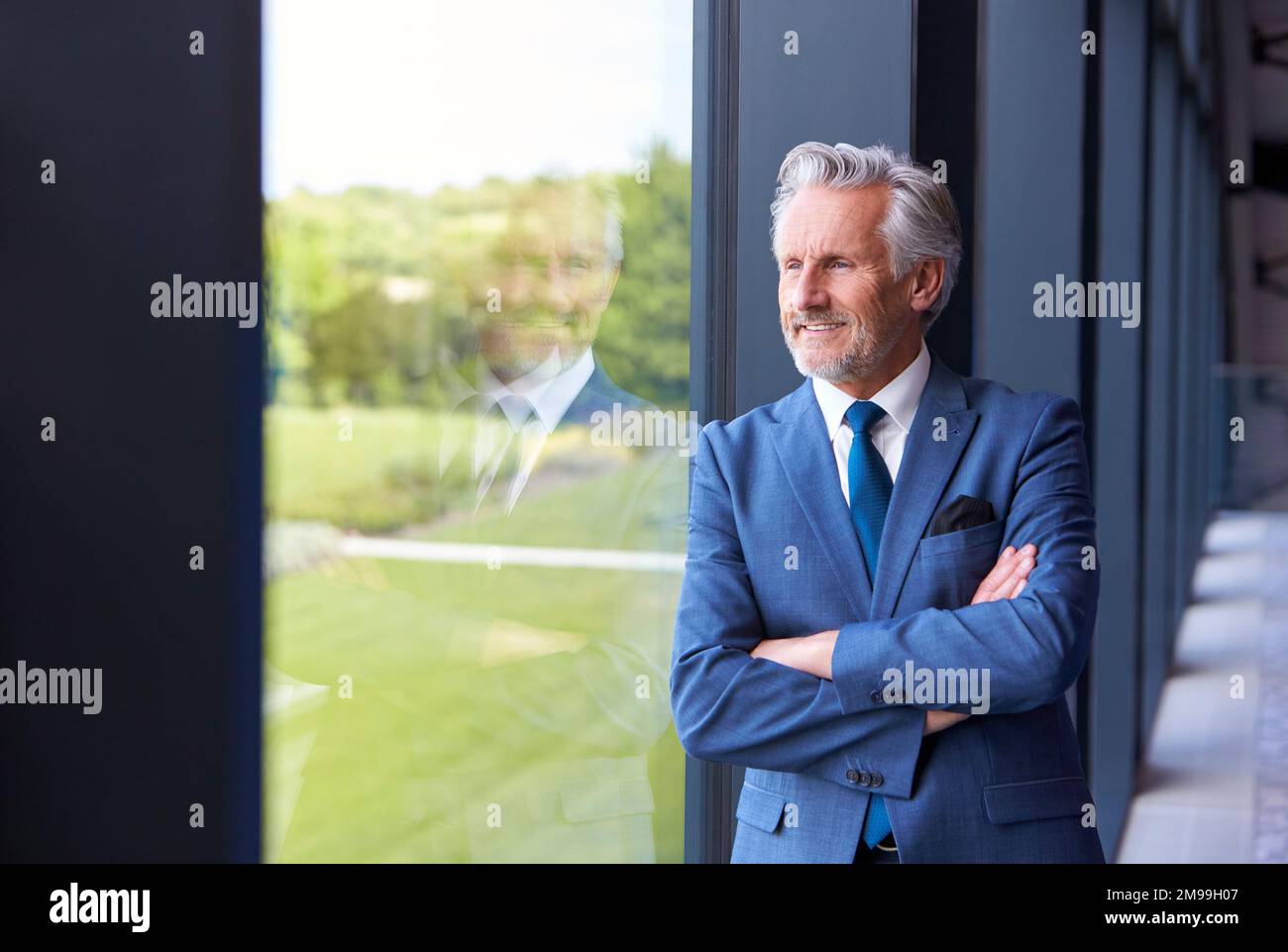 Portrait Of Smiling Senior Businessman CEO Chairman Standing By Window Inside Modern Office Building Stock Photo