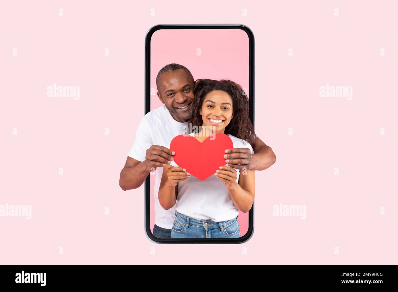 Love and care. Happy african american spouses hugging holding red paper card heart standing inside smartphone screen Stock Photo