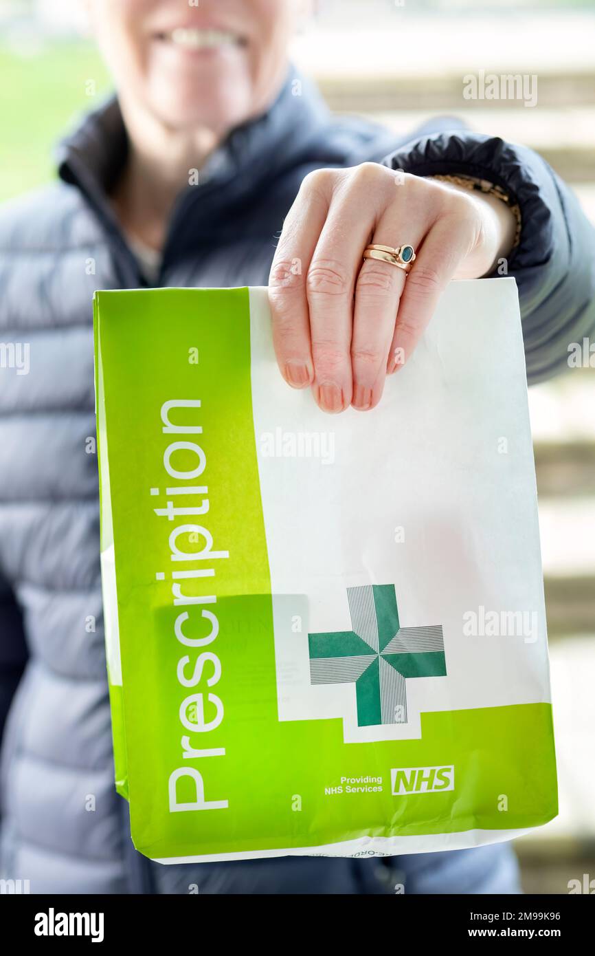 A patient holds up a recently dispensed medicine prescription in an NHS Prescription bag. The image clearly shows Prescription marked on the paper bag Stock Photo