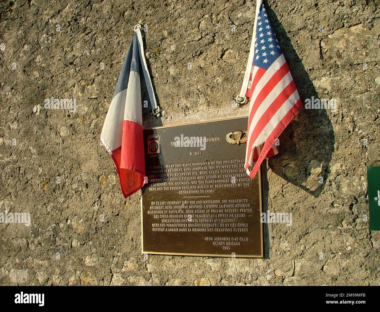 The plaque was erected by the 82nd Airborne C47 Club and commemorates the action of 'Company D' of the 2nd Battalion 505 Parachute Infantry Regiment, 82nd Airborne Division, in foiling a German attack on Ste Mere Eglise. It also acknowledges the help of the French in tending the wounded. After Normandy the 505th shoulder insignia carried the text 'H-MINUS' at the bottom because the Battalion jumped earlier than it should have done. Stock Photo