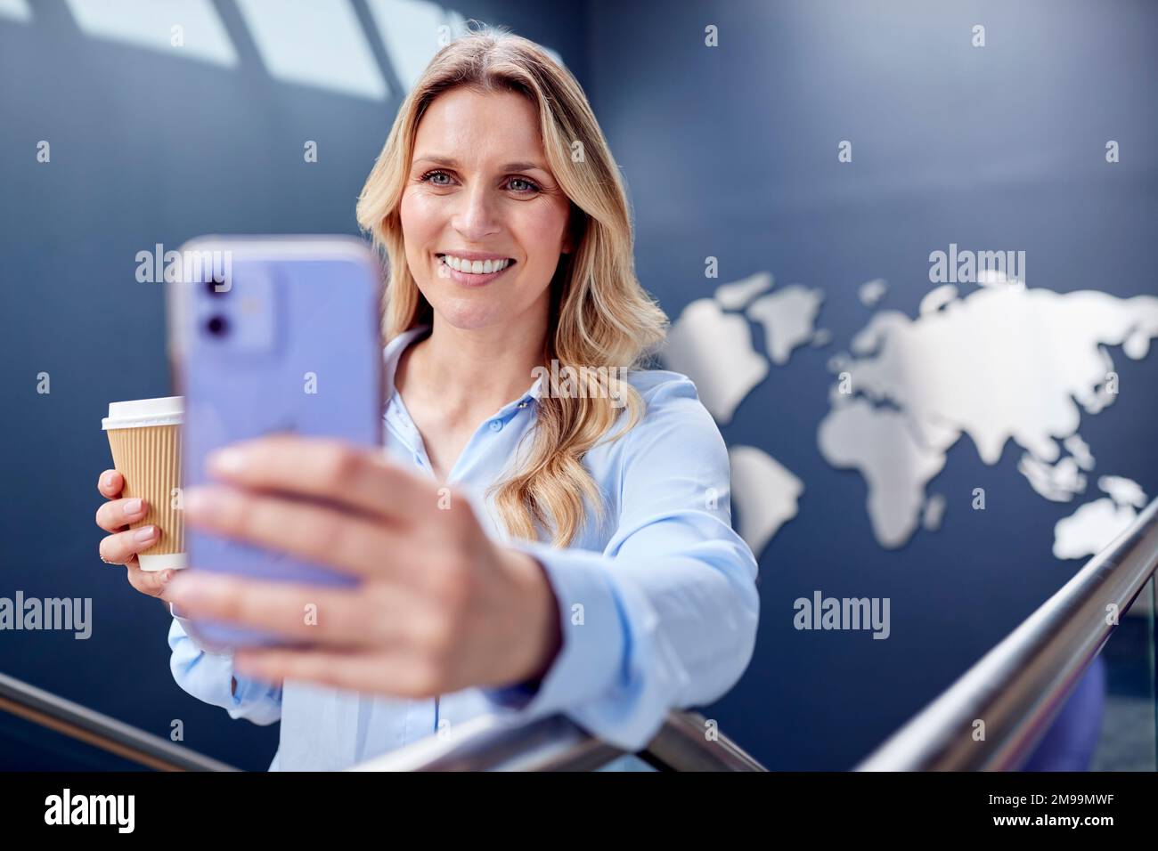 Businesswoman Looking At Mobile Phone Climbing Stairs Of Office With World Map In Background Stock Photo