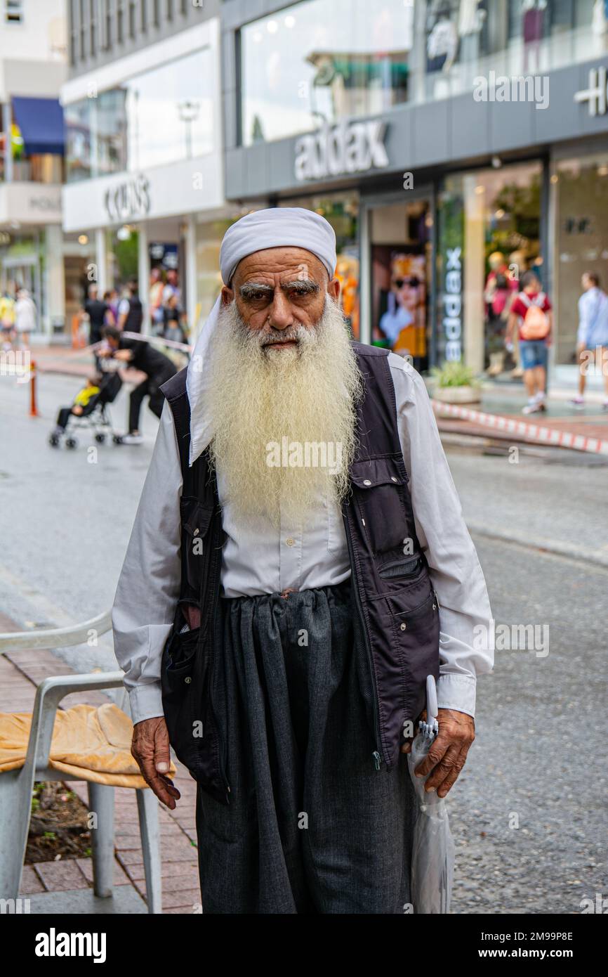 Alanya, Turkey, 16.10.2022: An old man with a long gray beard is dressed in Arabic style on the street of a Turkish city. A colorful man looks at the Stock Photo