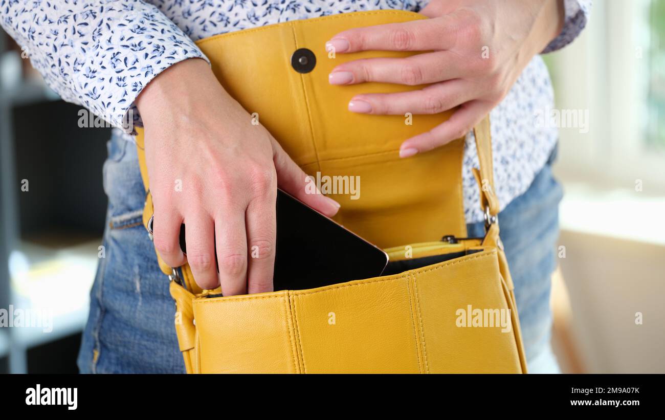 Woman puts her smartphone on yellow shoulder bag close up. Stock Photo