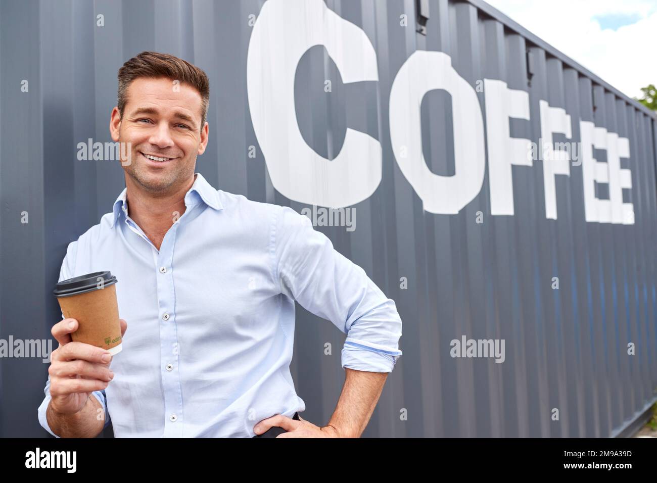 Portrait Of Male Owner Of Coffee Shop Or Distribution Business Standing By Shipping Container Stock Photo