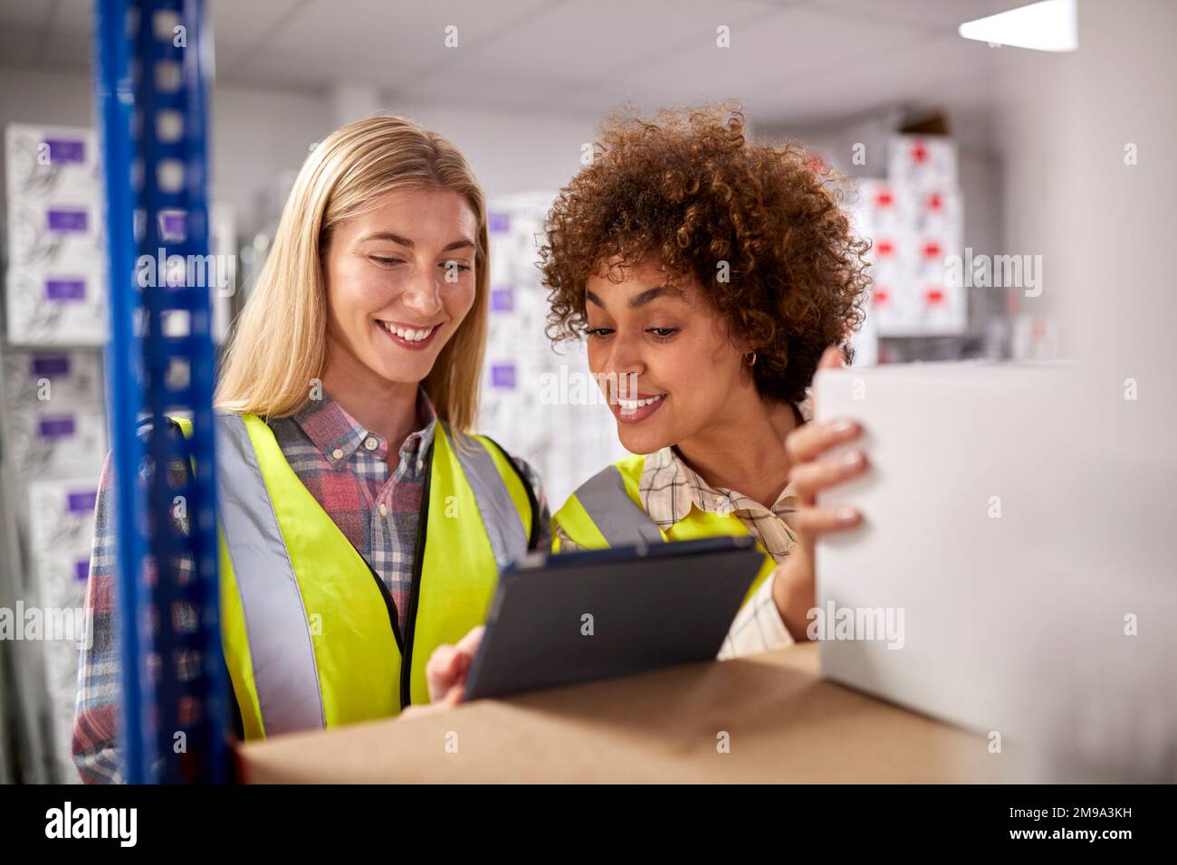 Two Female Workers In Logistics Distribution Warehouse Using Digital Tablet Stock Photo