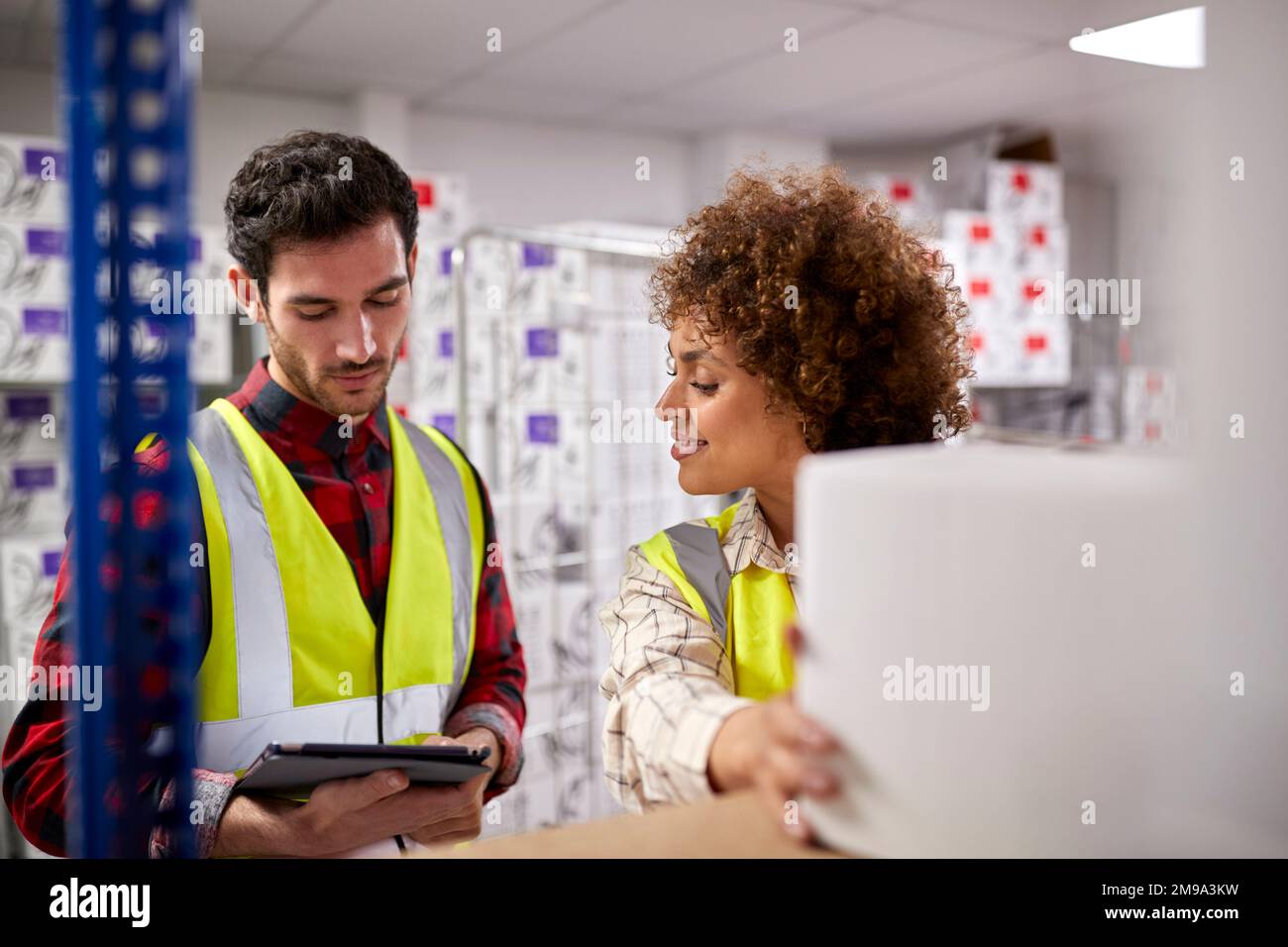 Male And Female Workers In Logistics Distribution Warehouse Using Digital Tablet Stock Photo